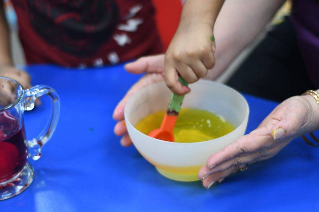 Child under IWC Care for the Newcomer Child program, preparing a yellow liquid with a red spoon