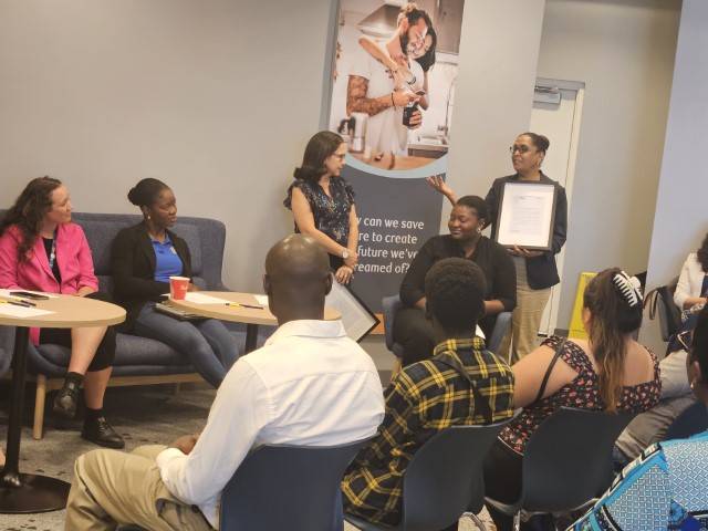 Elham Bakri standing and speaking at closing ceremony of RBC mentorship program. Participants are sitting with heads turned to listen to her remarks.